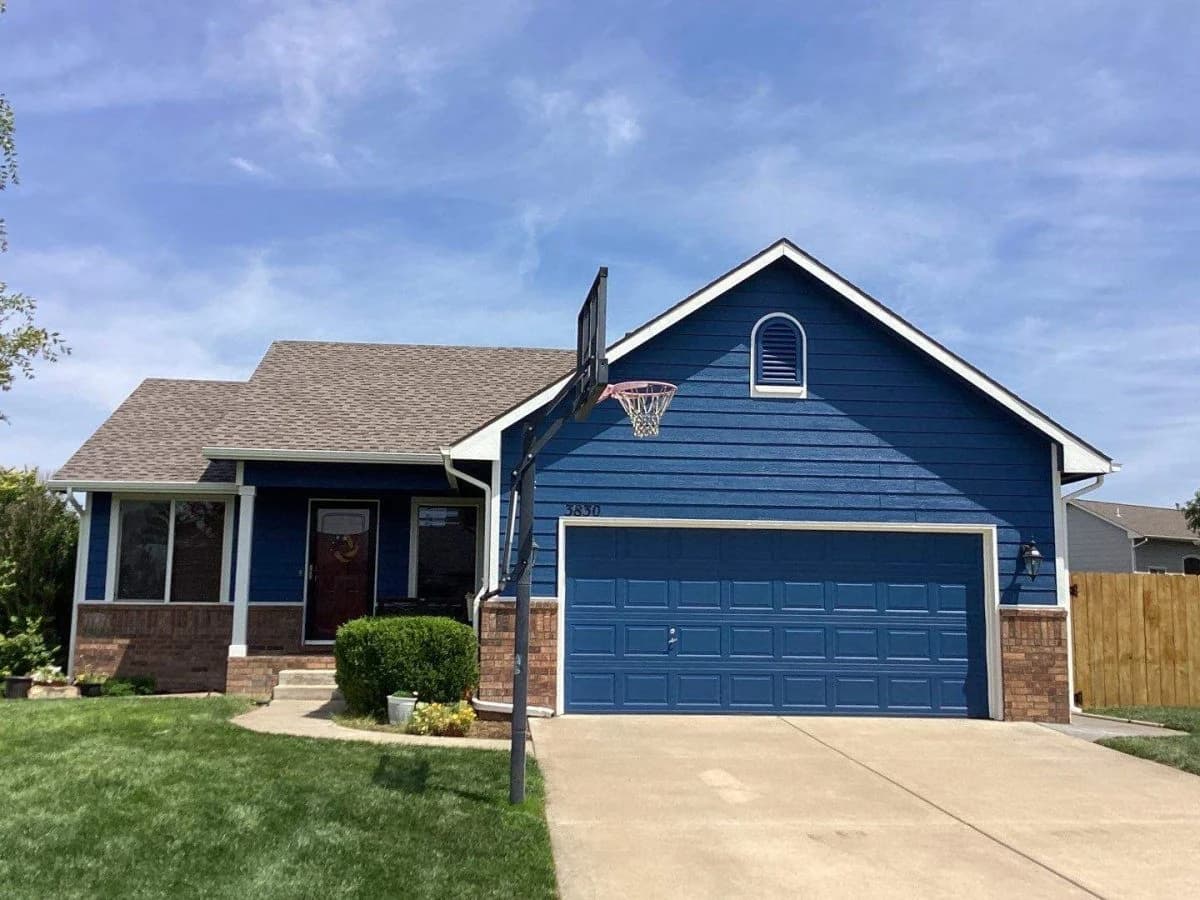 This is an image from River City Painting Inc. The image shows a blue single-story home in Wichita KS with fresh exterior paint and a brick accent base.