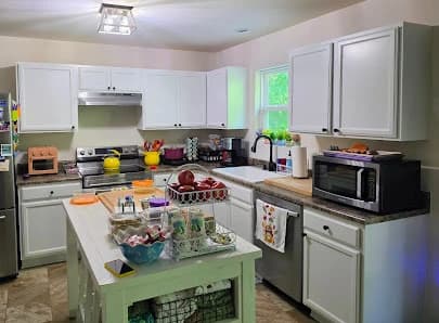 Kitchen painting project by CertaPro Painters of Fayetteville, NC in Lillington, NC. The image shows white cabinets, pale walls, and a green island.