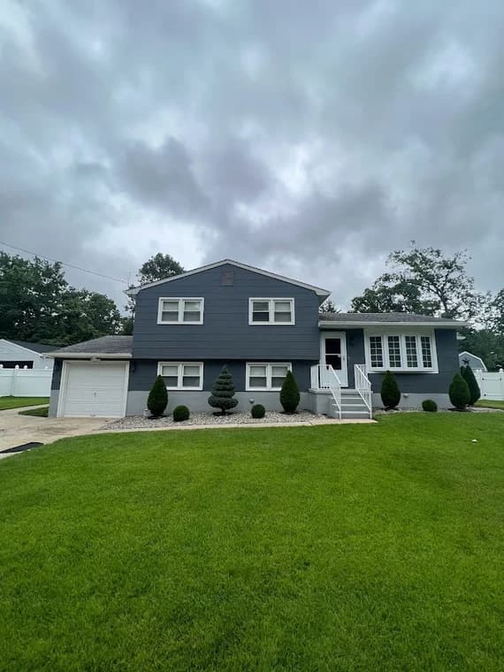 Exterior painting project by Brush Masters Painting Contractors LLC in Egg Harbor Township, New Jersey, featuring a dark blue house with white trim and landscaping.