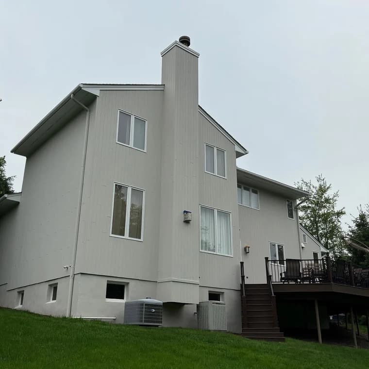 Exterior of a two-story home painted in a smooth neutral gray finish with white trim around windows and deck railing.