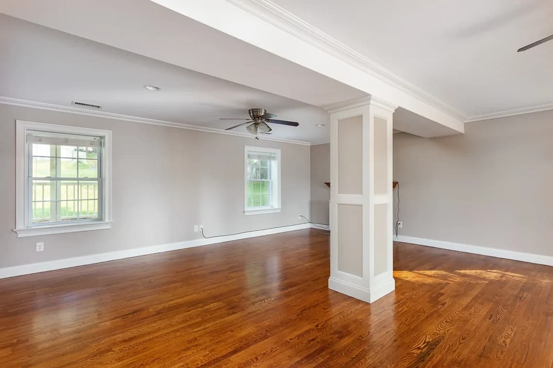 This is an image from KB Quality Painting, located in New York. The image shows a finished basement or living area with soft gray walls, white trim, recessed lighting, and polished hardwood floors.