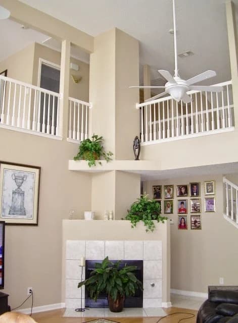 "This is an image from CertaPro Painters of Lake Ray Hubbard, located in Texas. The interior photo shows a tall living room with beige walls, white railings, a ceiling fan, and a tiled fireplace."