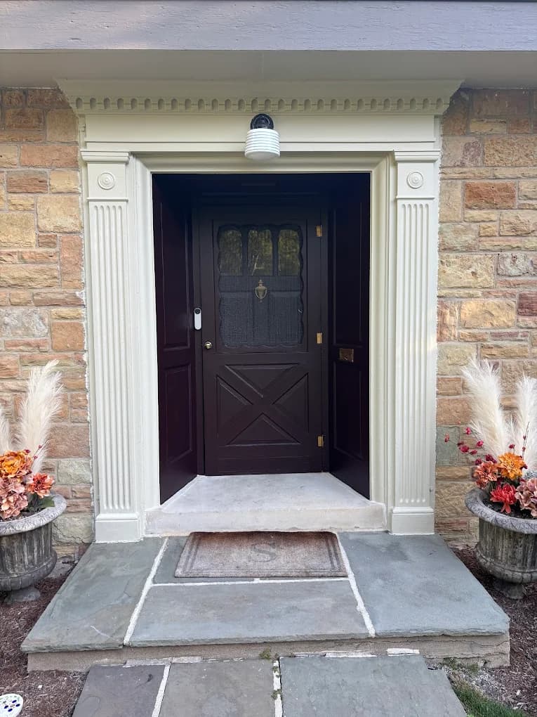 Exterior trim painting by Big League Painting in Glenview, Illinois. The image shows a dark front door, cream trim, stone siding, and planters.