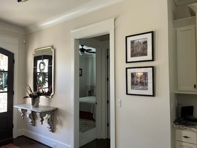 This is an image from Serious Business Painting LLC, located in Kentucky. The image shows a freshly painted interior hallway with light neutral wall colors, white trim, crown molding, framed wall art, and a clean, polished residential finish.