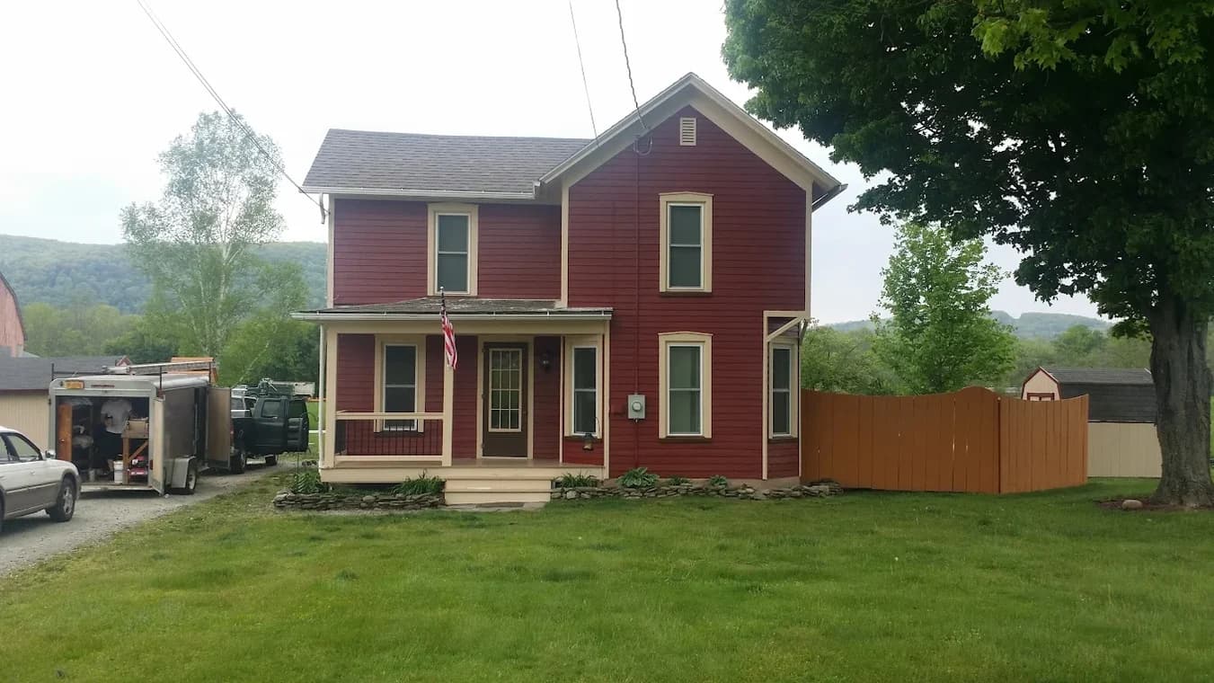 This is an image from A&L Painting, located in New York. The image shows a freshly painted red two-story farmhouse with cream trim and a covered front porch.