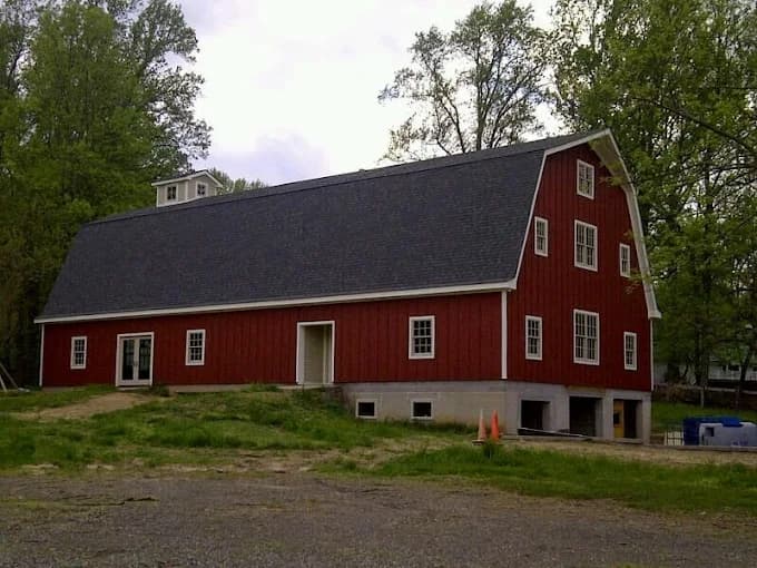 This is an image from CertaPro Painters of Columbia, located in Maryland. The image shows a large red barn-style building with white trim and a dark gray roof surrounded by green trees and grass.