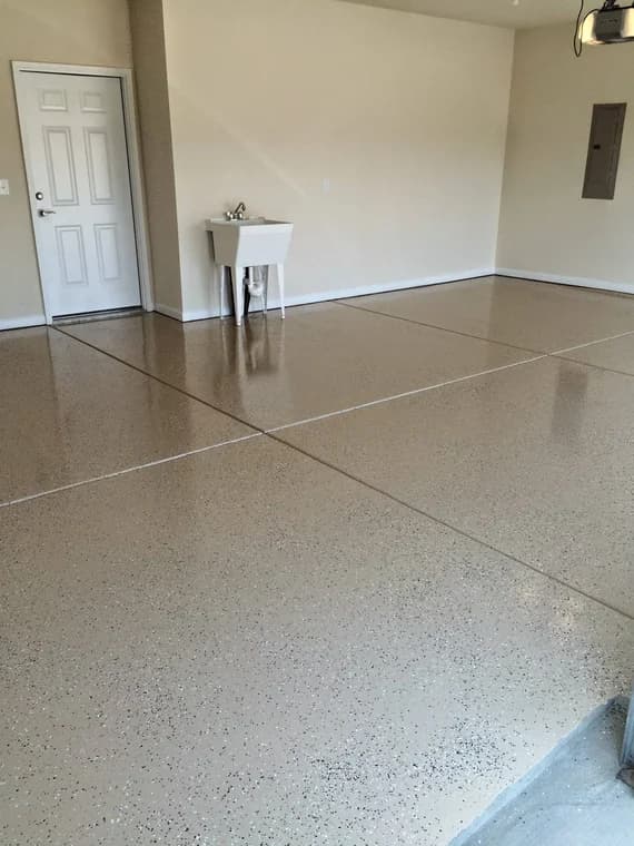 Garage floor coating project by Express Yourself Paint LLC in Raleigh, North Carolina. The image shows a tan speckled floor beside a utility sink and white door.
