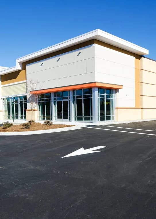 This is an image from Alarcon Pro Painting & Design, located in North Carolina. The photo shows a freshly painted commercial building with cream and beige walls, glass storefront windows, and a clean asphalt parking area marked with white lines.