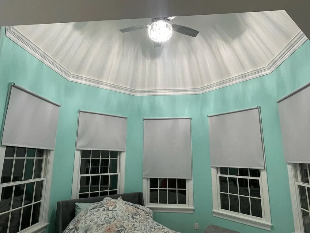 Bedroom with aqua-colored walls and a decorative ceiling, freshly painted by Romeo Painting Plus, LLC, including white trim and crown molding.