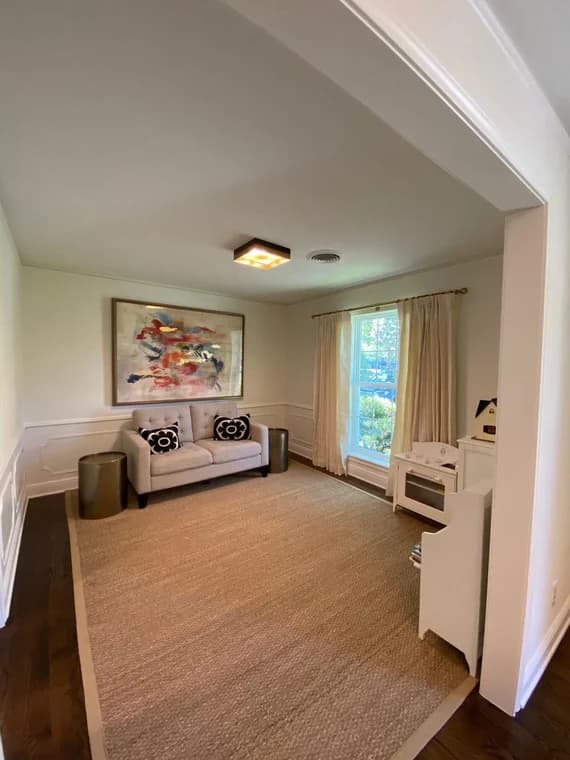 "This is an image from Squared Away Painting, located in Texas. The interior room displays newly painted soft neutral walls, a large abstract painting, and a small seating area with natural light from a front-facing window."