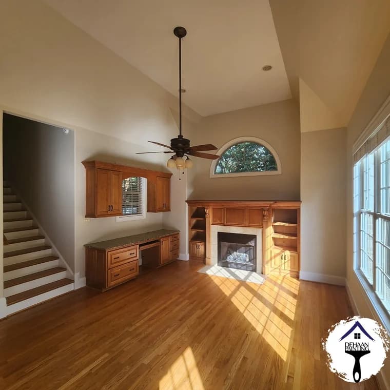 Interior painting project by DeHaan Painting in Charlotte, NC. The image shows a living room with tan walls, white trim, stairs, and a fireplace.