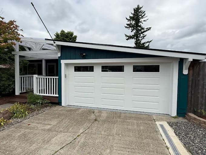 This is an image from Muir Painting Inc  company, located inHappy Valley, OR The image is a garage exterior painting by Muir Painting Inc featuring teal blue siding with bright white garage door and trim, enhancing curb appeal.