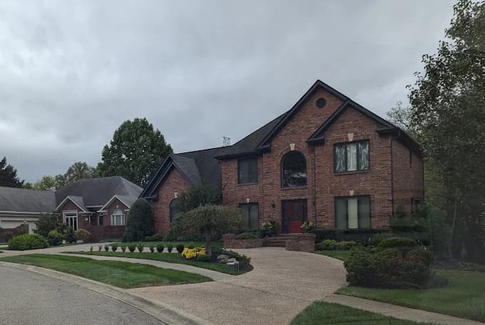This is an image from Serious Business Painting LLC, located in Kentucky. The image shows a large two-story brick home exterior with well-maintained landscaping and a clean, updated residential appearance.