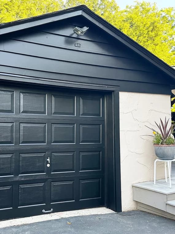 This is an image from That 1 Painter North Jersey. It highlights a freshly painted black garage with matching siding and door, paired with a light exterior wall.
