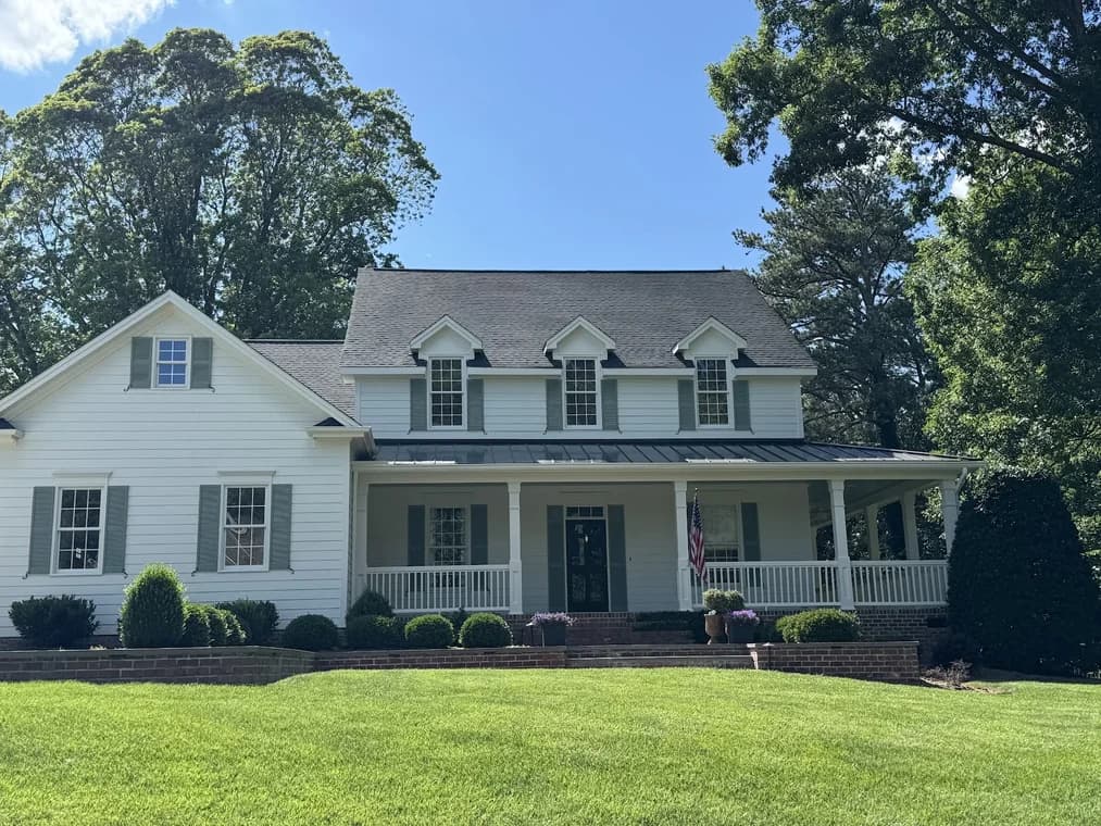 Exterior painting project by CPM Painting INC in Raleigh, NC. The image shows a white two-story home with gray shutters and a front porch.