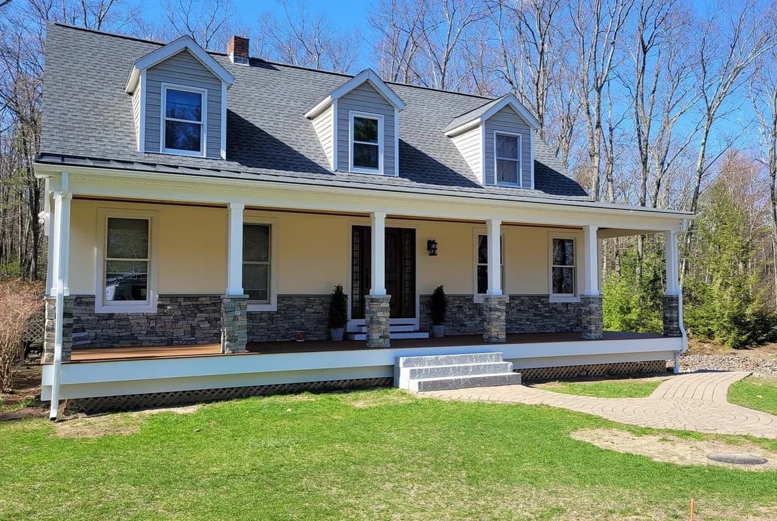 This is an image from EVM Home Improvement & Painting, located in Massachusetts. The photo shows a renovated home with cream-colored siding, stone accents on the lower exterior, and a large front porch with white columns.