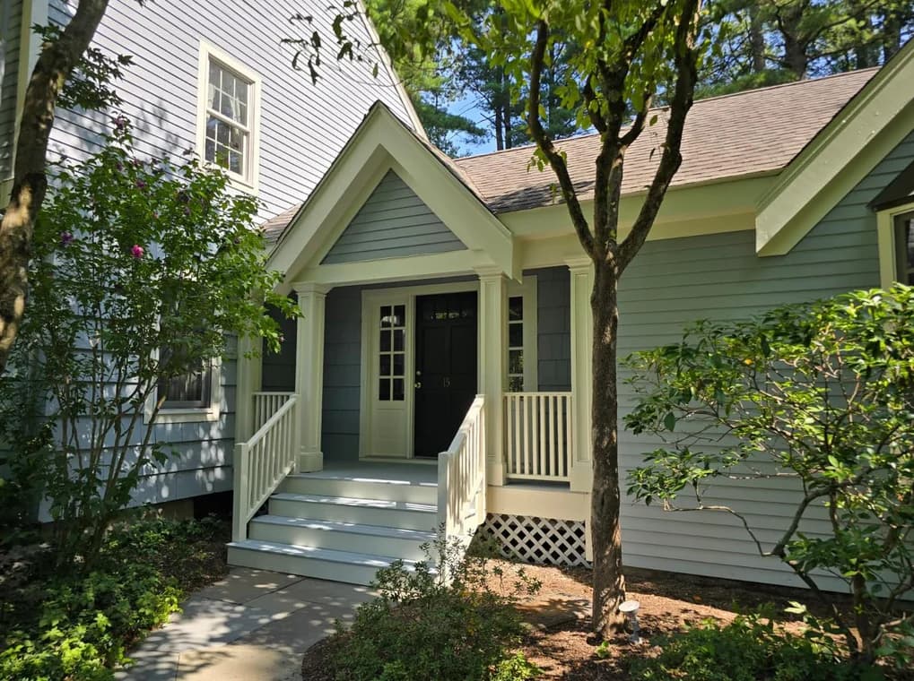 This is an image from Right Track Painting & Sealcoating, showing the entrance of a home with light gray siding and white trim. The front steps and porch railings are freshly painted, enhancing the home’s curb appeal.