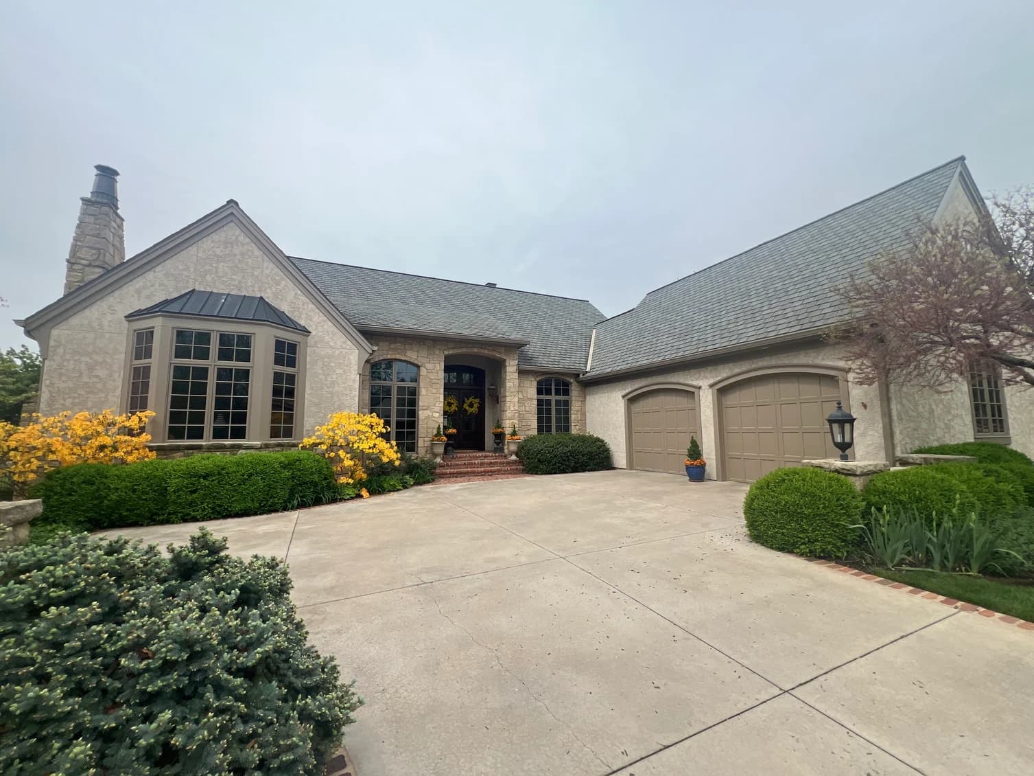 This is an image from Graystone Painting and Refinishing. The image is an exterior home in Kansas City KS with painted stucco walls, stone accents, and freshly refinished garage doors.