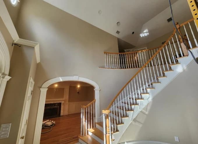 This is an image from Teall Painting, located in Michigan. The image shows a freshly painted interior stairwell and entryway with neutral wall colors, white trim, and a curved wooden staircase.