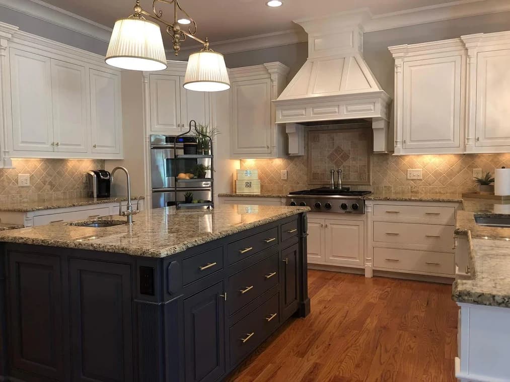 Cabinet painting project by Anderson Painting in Raleigh, North Carolina. The image shows white cabinets, a navy island, brass hardware, and tile backsplash.