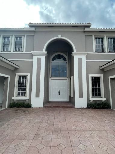 This is an image from Precision Painting Plus of Suffolk County, located in New York. The photo shows a freshly painted two-story home exterior featuring gray walls with white trim and a large arched entryway.