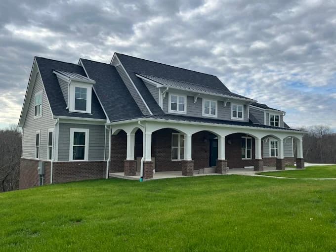 This is an image from Skywalkers Painting & Repairs, located in Ohio. The image shows a large two-story home exterior with gray siding, brick accents, white trim, and a covered front porch after exterior painting.