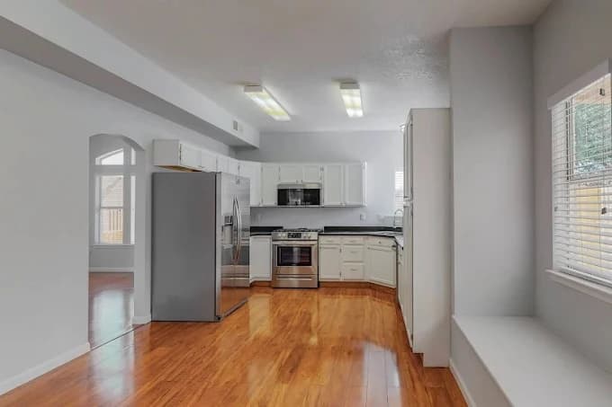 This is an image from Straight Line Painting LLC, located in New Mexico. The photo shows a bright modern kitchen with freshly painted white cabinets, stainless steel appliances, and polished wood floors.
