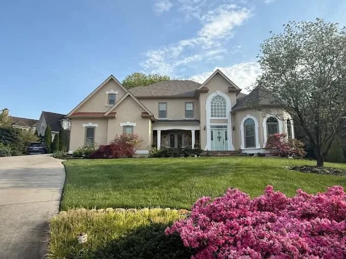 This is an image from That 1 Painter Knoxville, located in Tennessee. The image is a beautiful two-story beige home with white trim and manicured lawn freshly painted by That 1 Painter Knoxville.