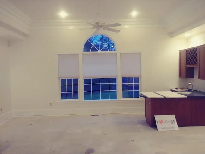 This is an image from Castle Complements Painting Co., located in Massachusetts. It displays a freshly painted interior living room with white walls, a large arched window, and recessed ceiling lights.