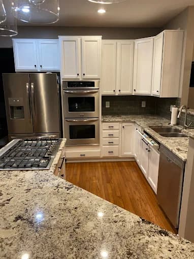 This is an image from Advantage Paint Services, located in New York. The image shows a modern kitchen with white painted cabinets, granite countertops, stainless steel appliances, and hardwood flooring.