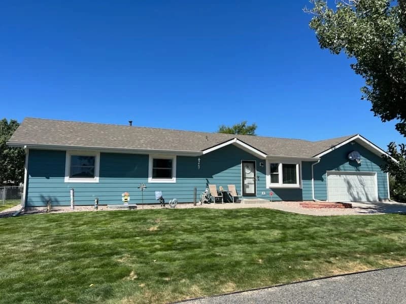 This is an image from Pro Classic Painting company, located in Aurora, CO The image is a freshly painted blue ranch-style home with white trim and light gray shingle roof, showcasing professional exterior residential painting by Pro Classic Painting