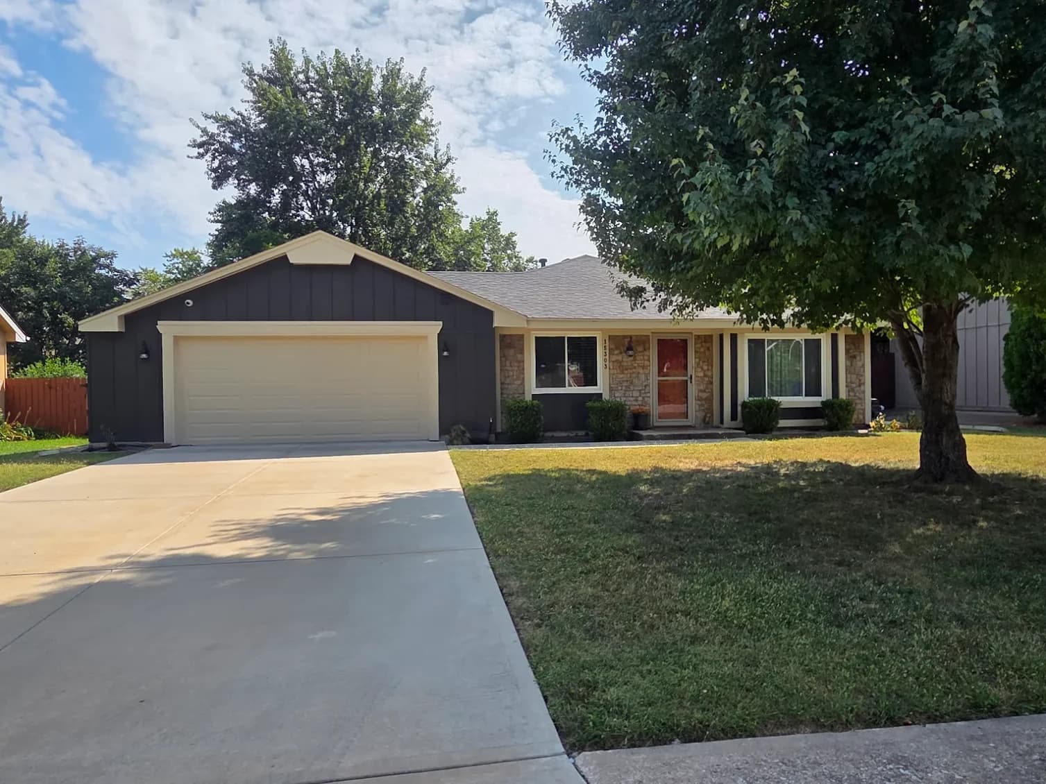 This is an image from 360 Painting of Overland Park. The image shows the exterior of a ranch-style home with a dark-painted facade, contrasting light trim, a stone accent section near the front door, and a well-maintained lawn and driveway.