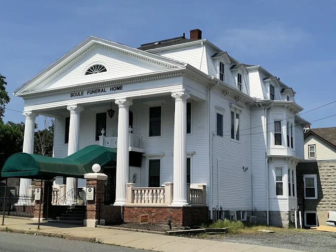 This is an image from CertaPro Painters of Attleboro, MA. It features a classic white building with tall columns and an arched green awning, painted with crisp white finishes.