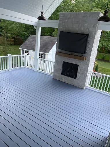 This is an image from 216 Painting, located in Ohio. The image shows a freshly painted two-story home exterior with light neutral siding, dark garage doors, a modern wood front door, and a spacious front deck surrounded by mature trees.