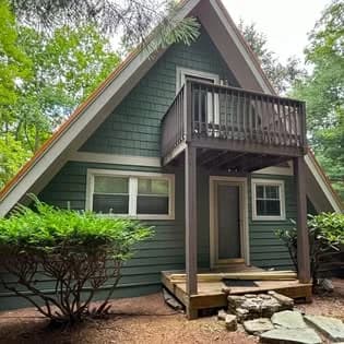 Exterior painting project by Passion Painters in Swannanoa, NC. The image shows a dark green A-frame home, brown balcony, tan door, and white trim.
