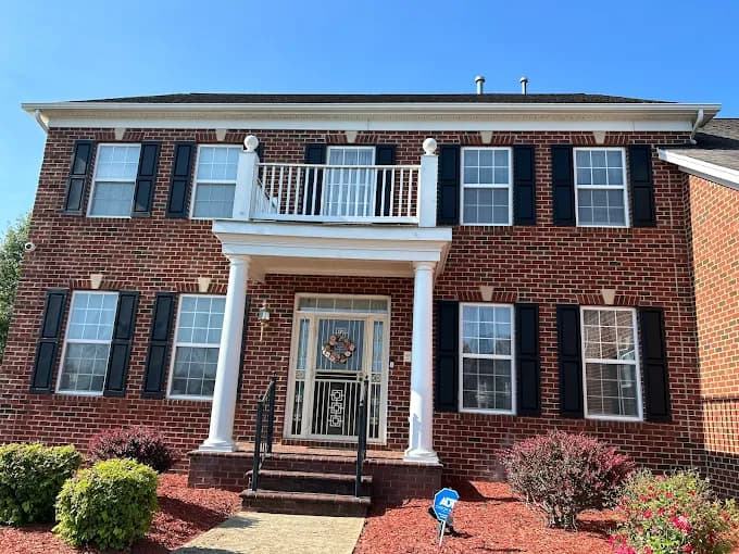 This is an image from C & V Painting Services LLC, located in Virginia. The exterior image shows a red brick two-story house with white pillars, black shutters, and neatly manicured shrubs in the front yard.
