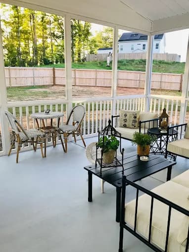 Porch painting project by NC Paint & PowerWash in Garner, North Carolina. The image shows a covered porch with white floor, railings, chairs, and plants.