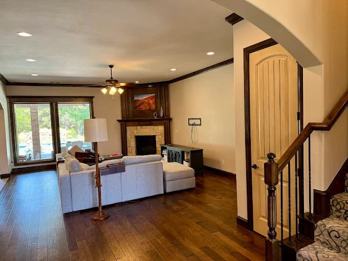 This is an image from Whitehead Brothers Painting, located in Oklahoma. The photo shows a freshly painted living room with cream-colored walls, dark wood trim, hardwood floors, and a stone fireplace accented by a modern sectional sofa.