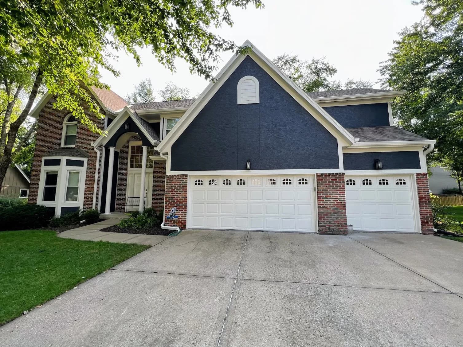 This is an image from Stack Painting. The image is exterior house painting in Kansas City KS showing a blue and brick two-story home with fresh contrasting trim and a clean, updated facade.