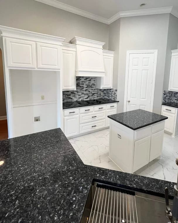 This is an image from Yellow Rose Painting, located in Texas. The kitchen showcases white cabinets, dark granite countertops, a gray tile backsplash, and polished white flooring.